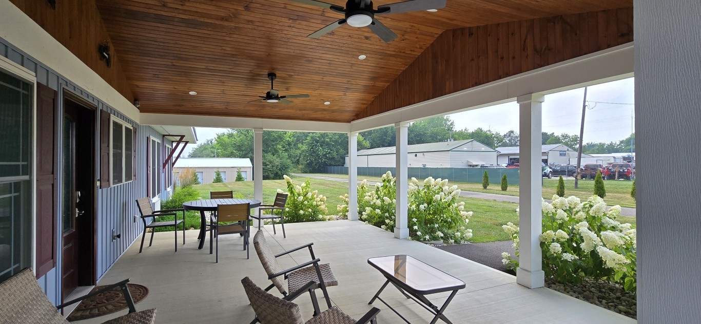 20260717_161959 - London Guest House Covered patio with a wooden ceiling and ceiling fans, outdoor table and chairs, and white hydrangeas along the edge overlooking a lawn.