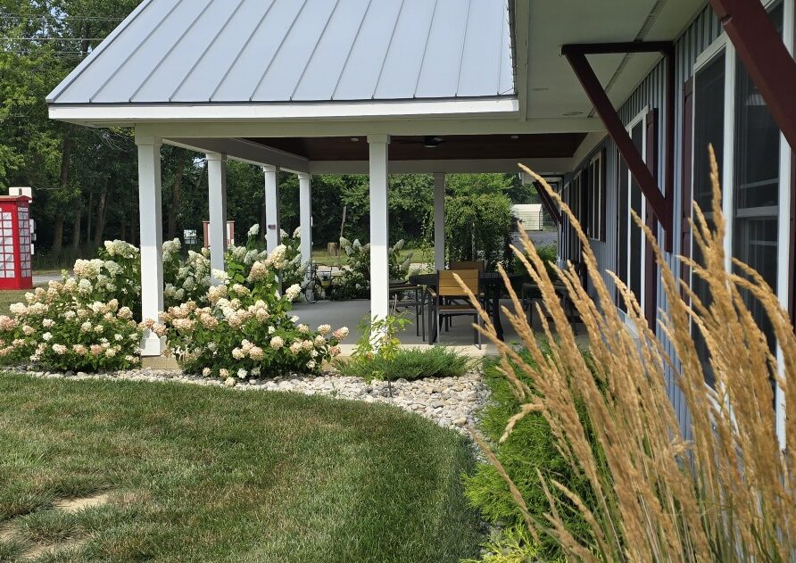 Exterior view of a building with a covered patio, white hydrangea bushes, and tall ornamental grasses in the foreground.